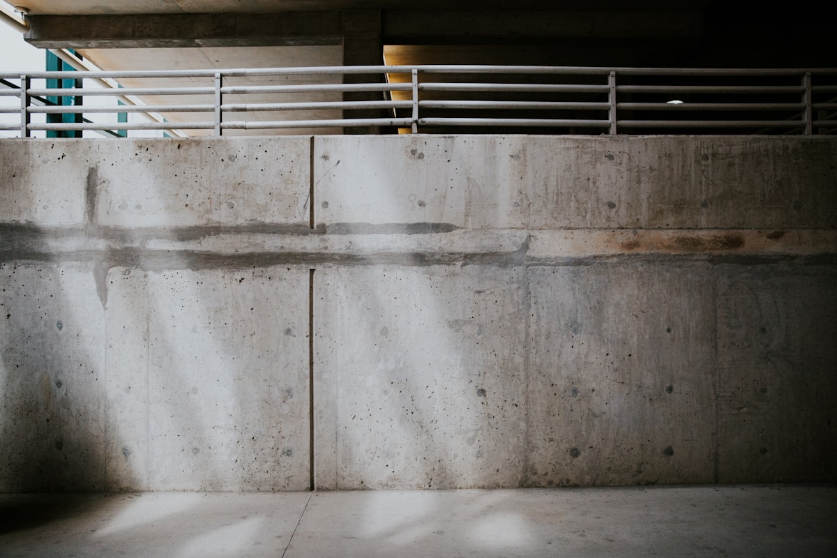 A plain metal railing running along the top of a blank concrete wall.