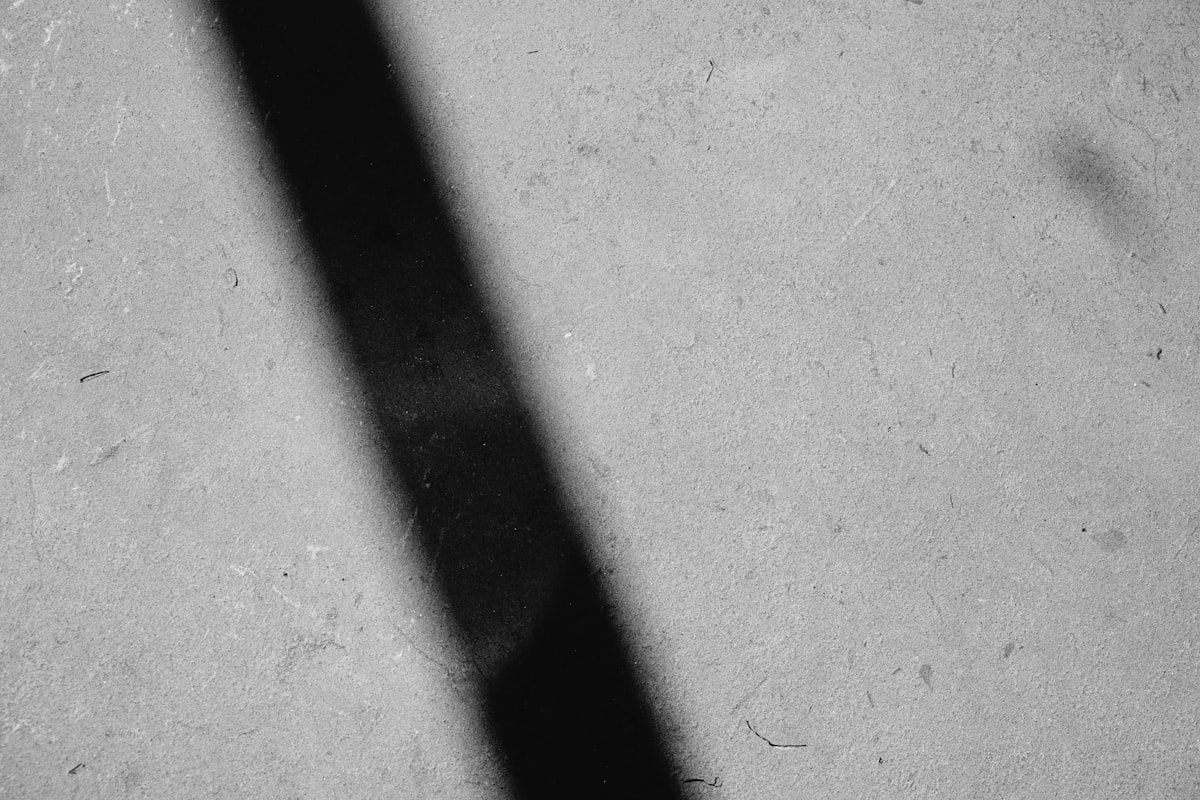 A single hard diagonal shadow falling across a flat grey concrete surface.