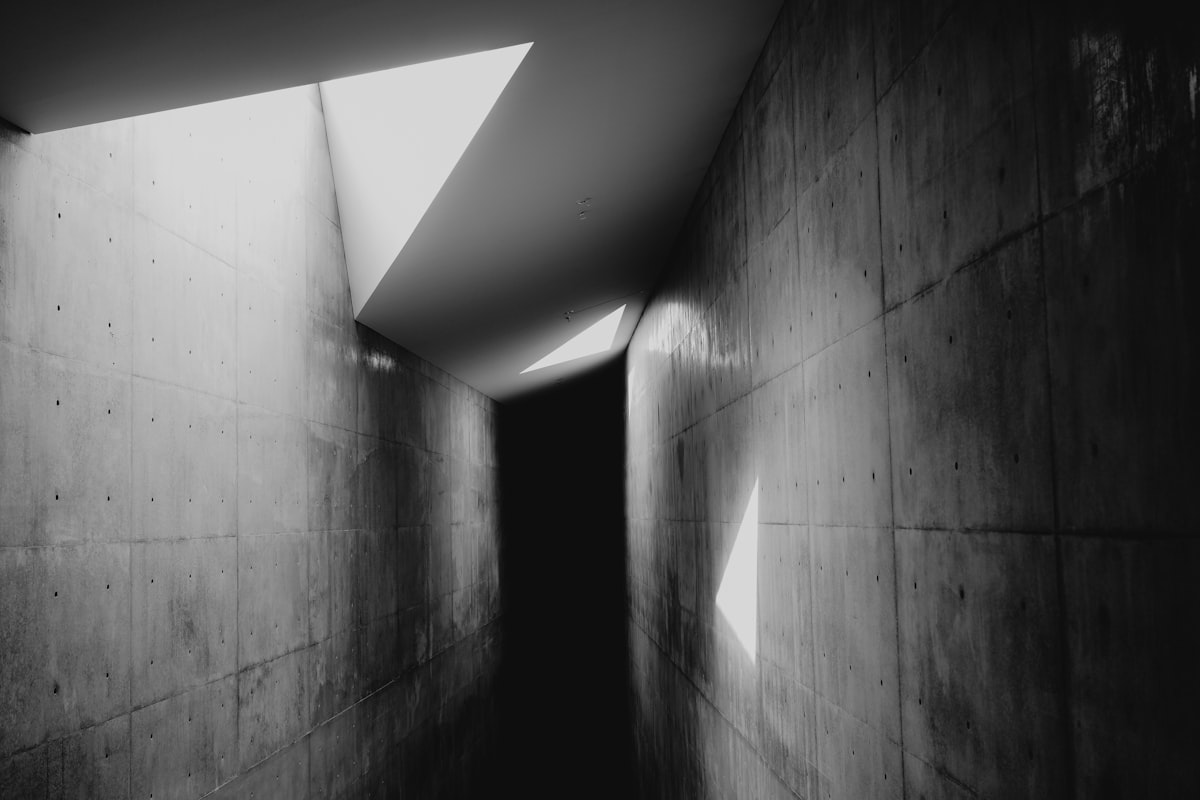 A concrete passage lit from one end, the light falling in a hard band across the floor.